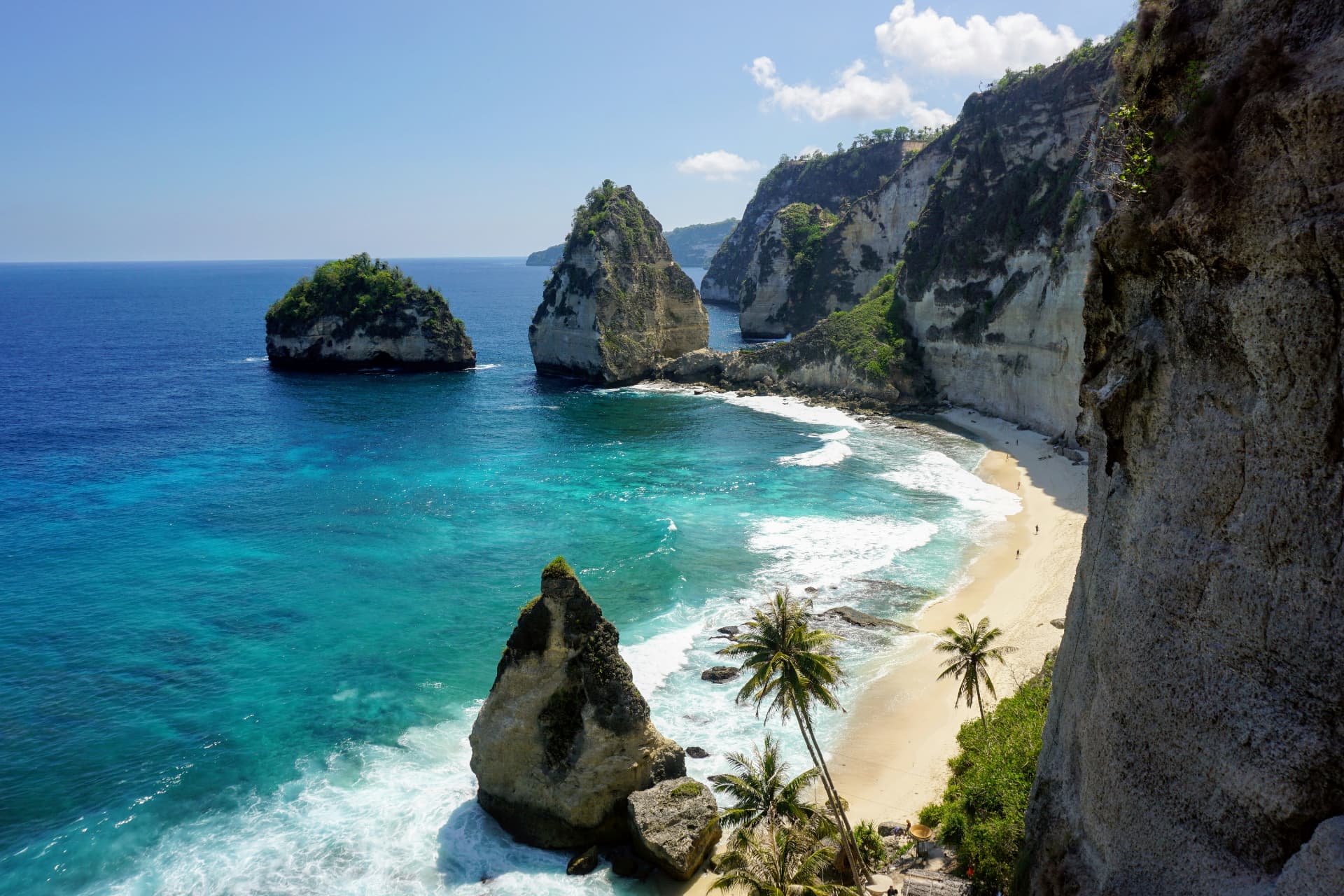 Turquoise ocean breaking on a white limestone cliff and palm-lined beach in Bali